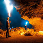 Explorers with flashlights in cave near fire and sunlight beam