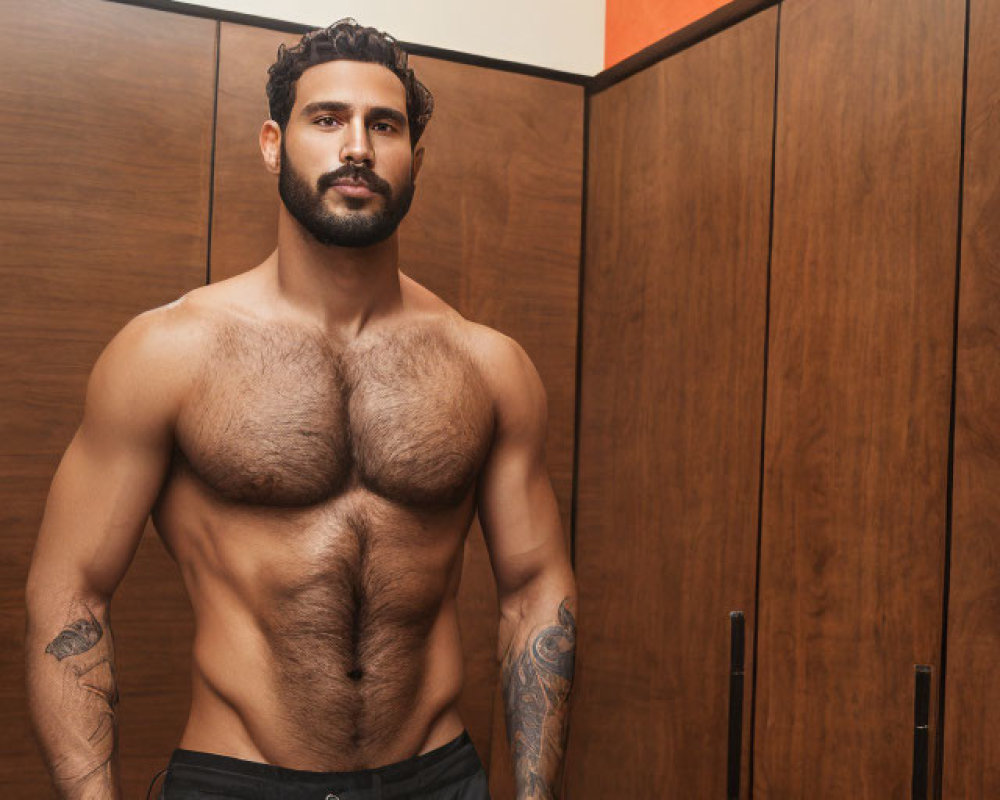 Muscular man with tattoos stands confidently in front of wooden locker background