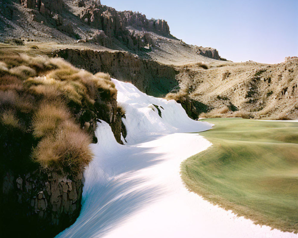 Snow-covered golf course nestled among rocky terrain and grassy knolls under clear sky