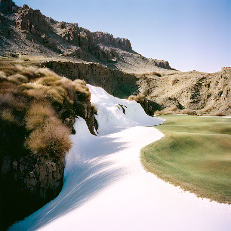 Snow-covered golf course nestled among rocky terrain and grassy knolls under clear sky