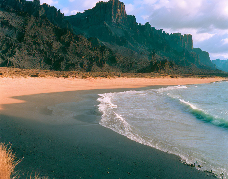 Scenic black sand beach with gentle waves, mountains, and blue sky