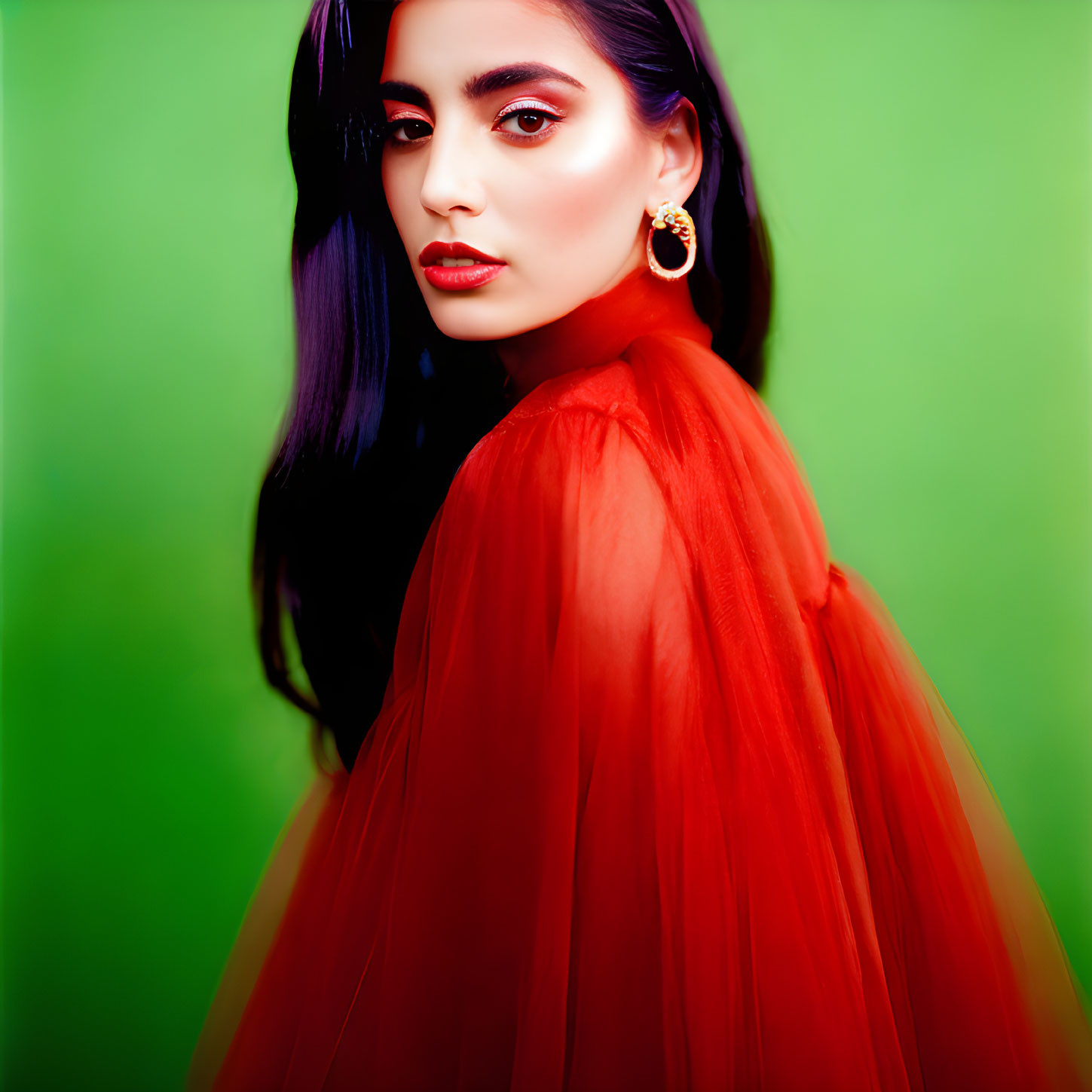 Dark-haired woman in red sheer garment and hoop earrings against green background