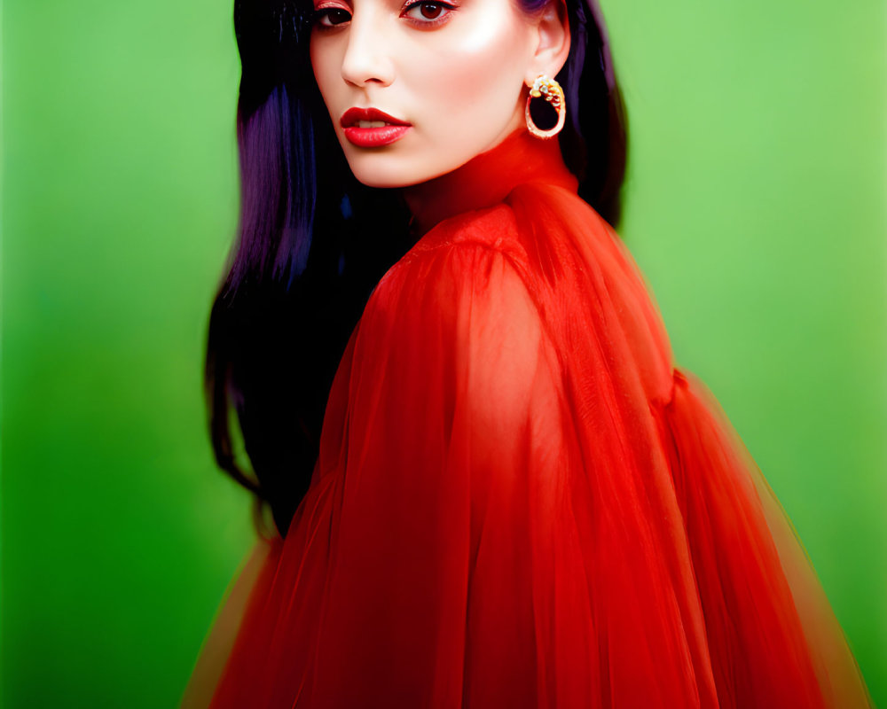 Dark-haired woman in red sheer garment and hoop earrings against green background