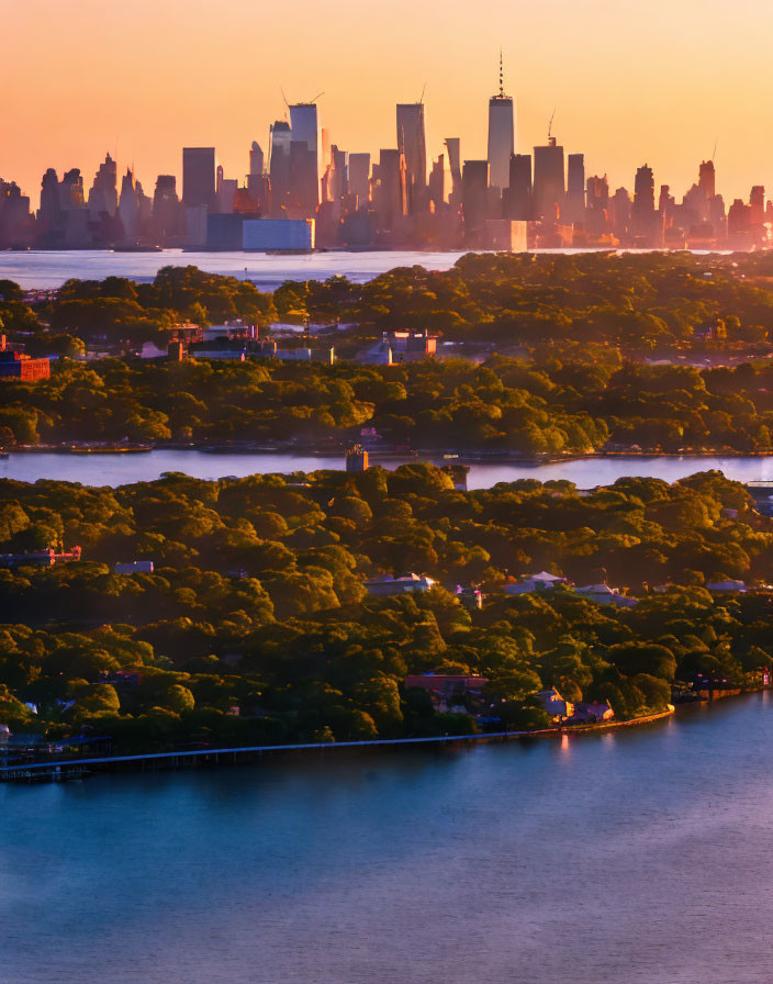 City skyline at sunset with green trees, river, skyscrapers in golden light.