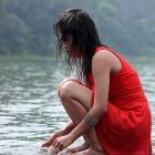 Woman in red dress by water with floating flowers and trees in serene setting