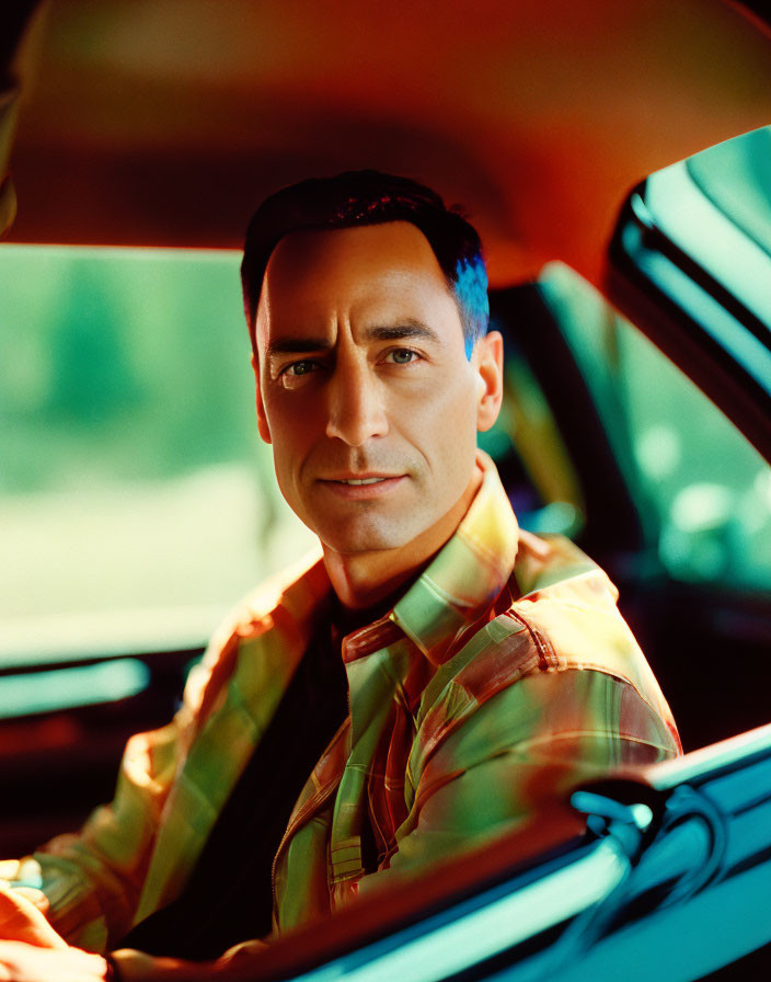 Dark-Haired Man Smiling in Striped Shirt in Car Seat with Sunlight