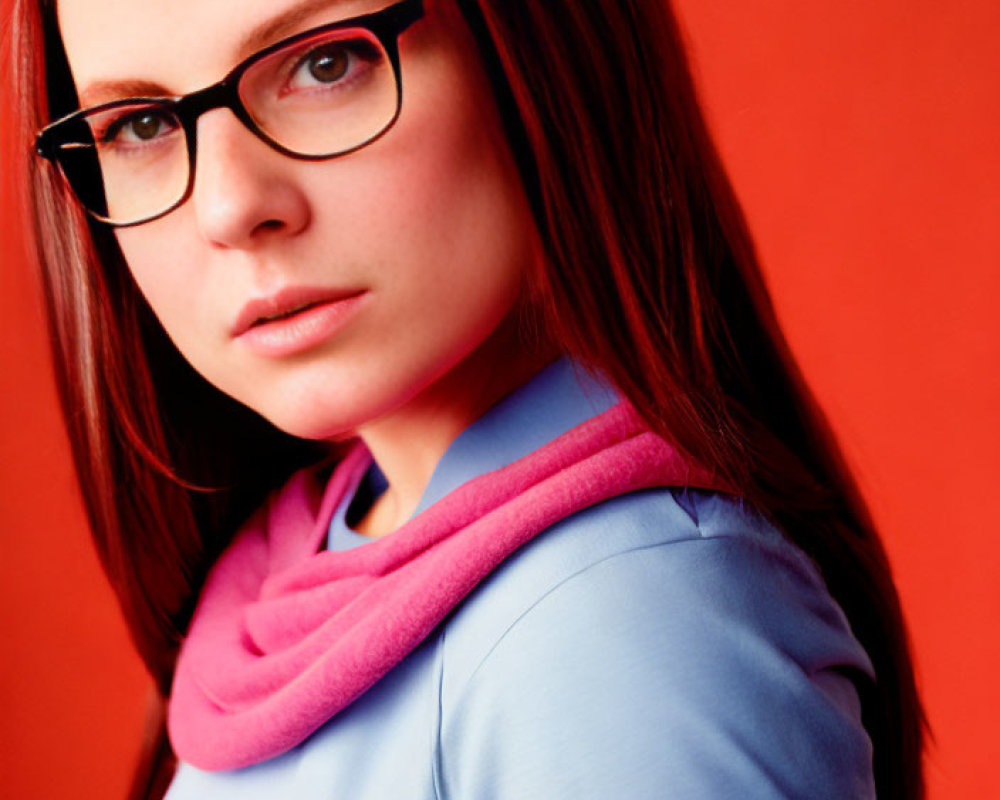 Woman in glasses with blue top and pink scarf on red background