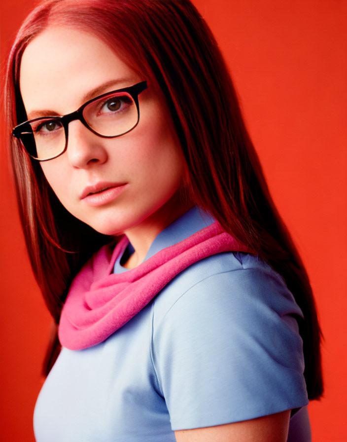 Woman in glasses with blue top and pink scarf on red background