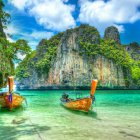 Scenic view of traditional longtail boats on turquoise water by rugged cliff