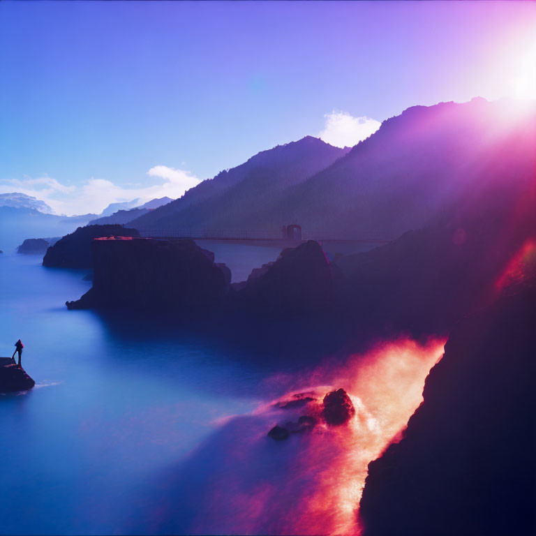 Silhouetted figure on rock gazes at misty seascape with mountains under sunset