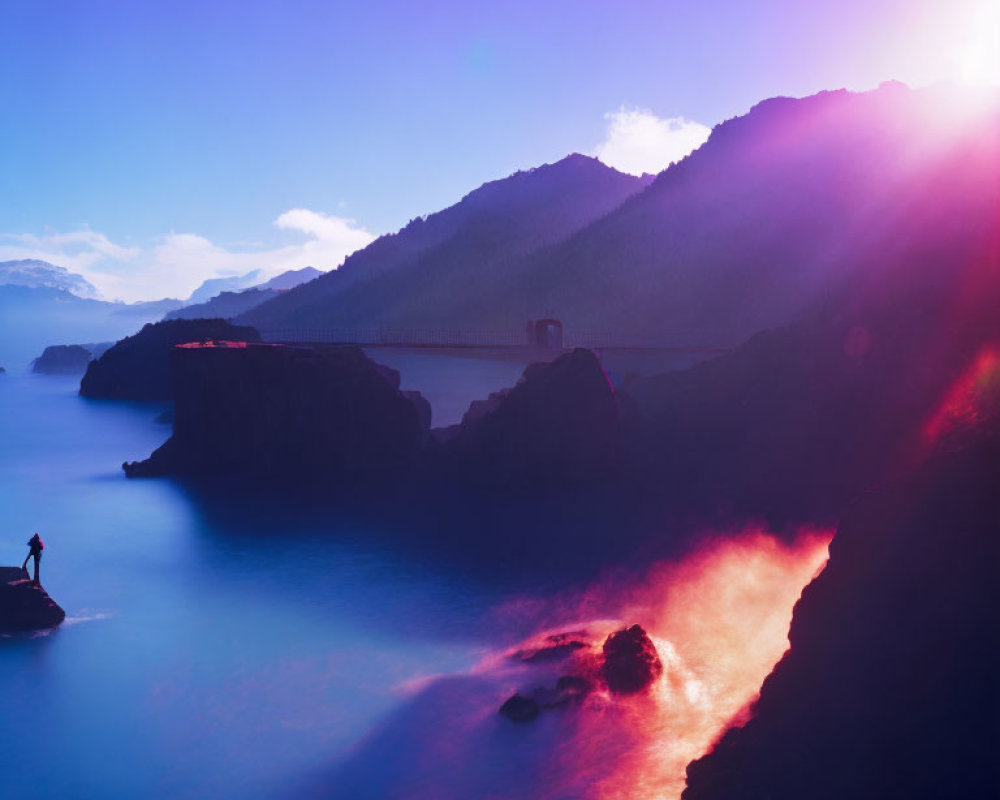 Silhouetted figure on rock gazes at misty seascape with mountains under sunset