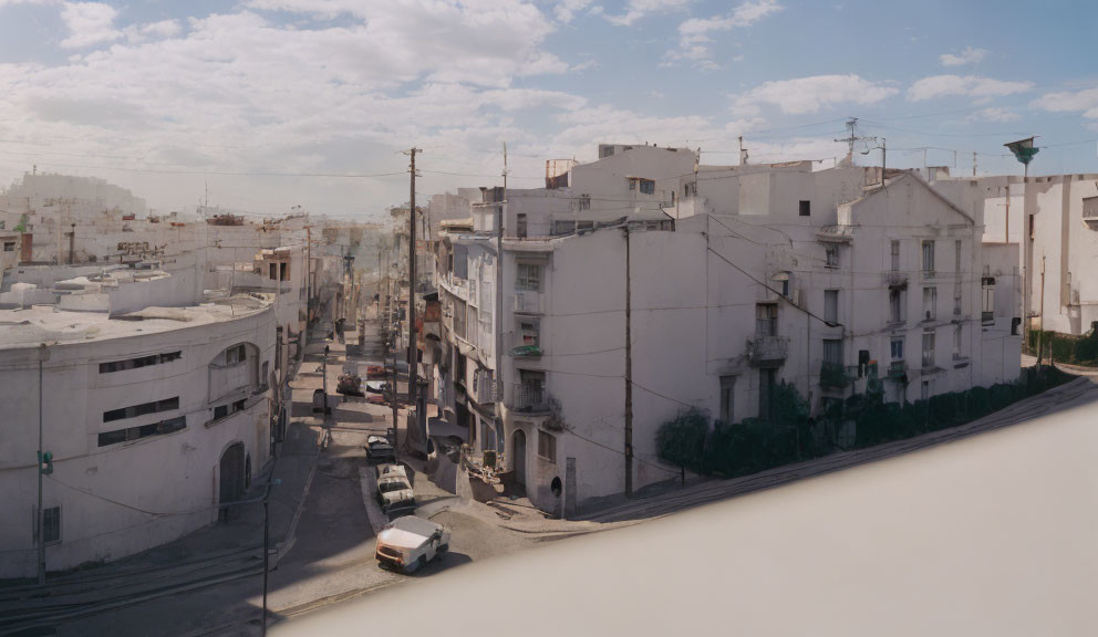 Quiet urban street with white buildings and parked cars under cloudy sky