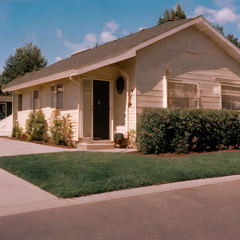 Beige single-story house with white trim and neat lawn under blue sky