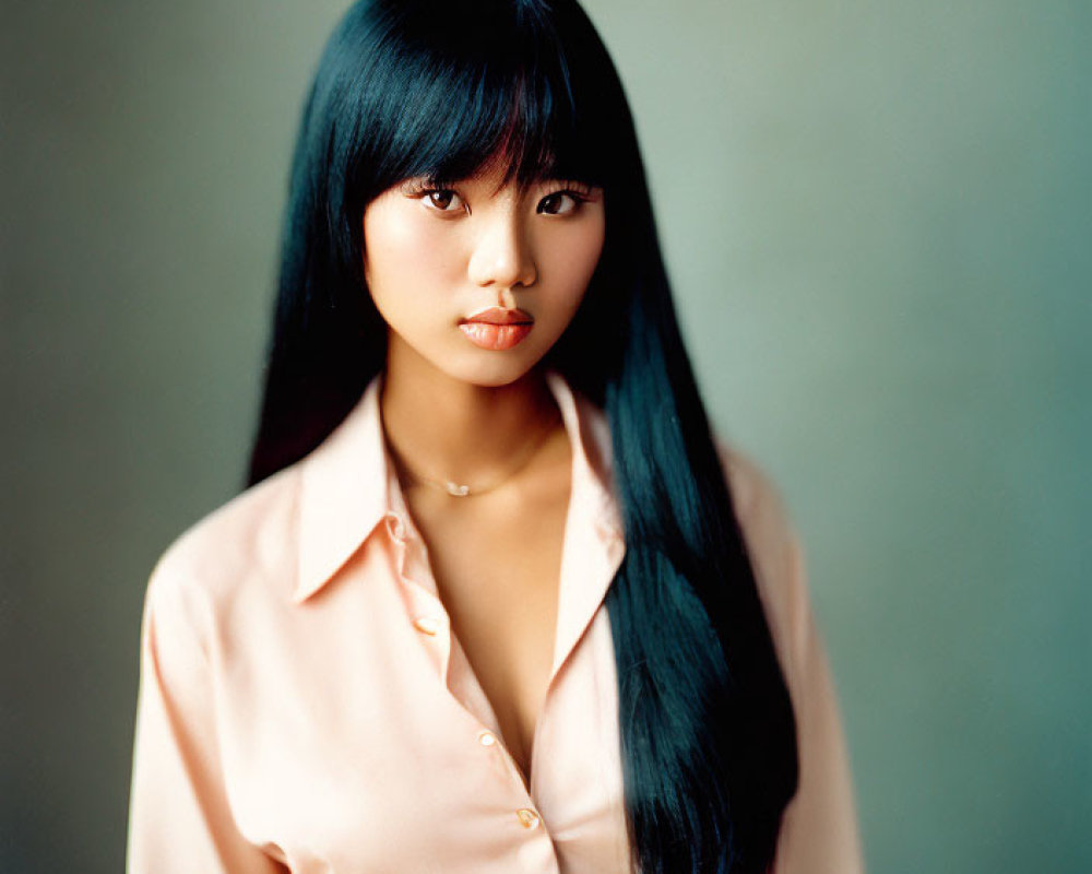 Long-haired woman in pink blouse with neutral expression.