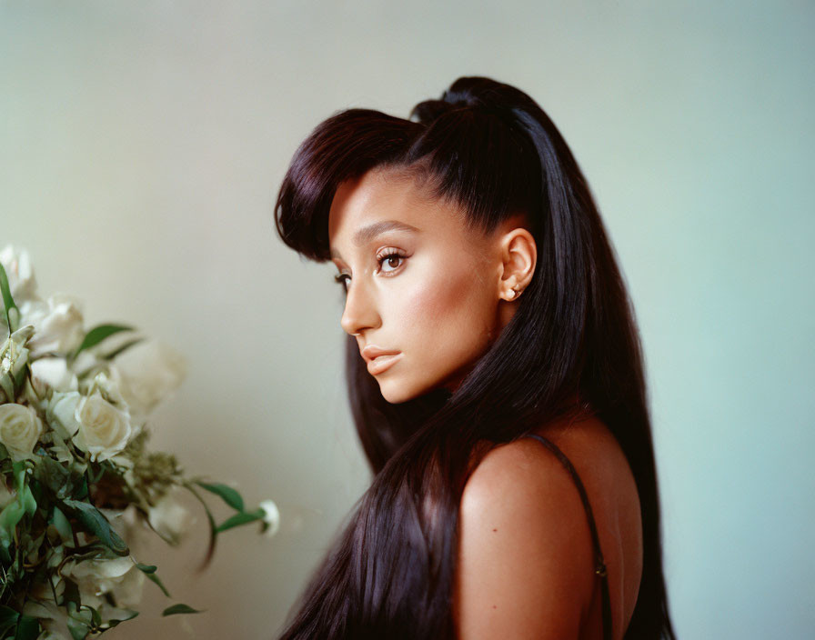 Profile of woman with high ponytail and wavy hair, holding white roses bouquet.