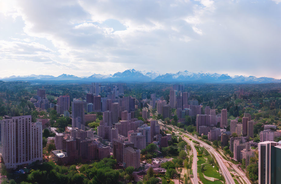 City skyline with high-rise buildings, greenery, road, mountains, and cloudy sky.