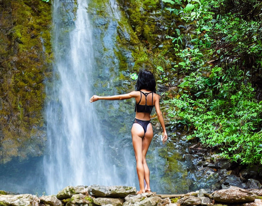 Bikini-clad person on rock near cascading waterfall