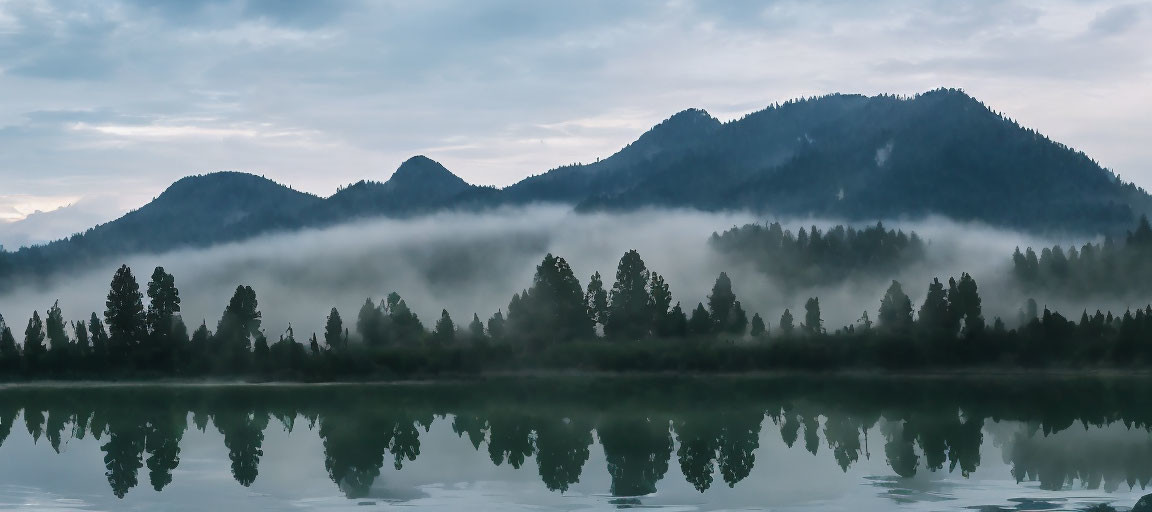 Misty forested mountains reflected on a calm lake at dawn or dusk