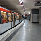 Modern subway station with white and orange trains under overhead lights.