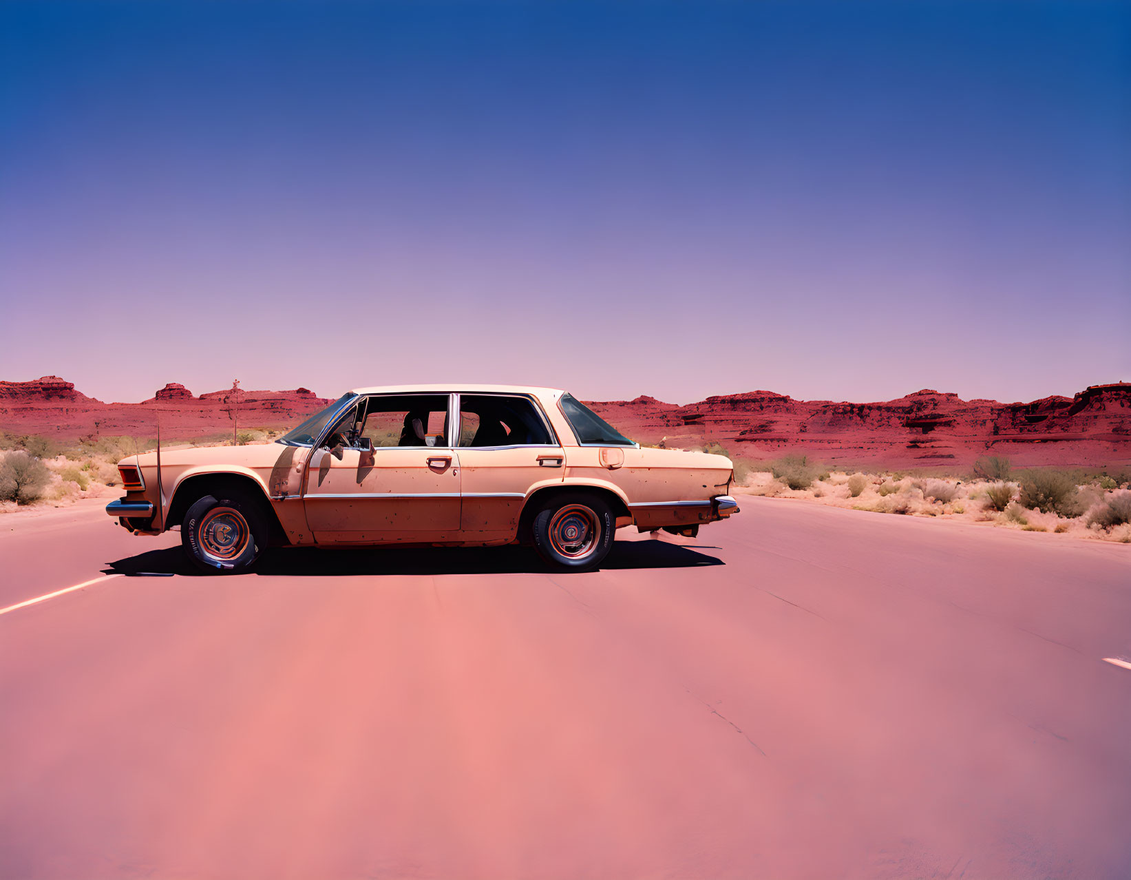 Vintage car on desert road with rocky backdrop