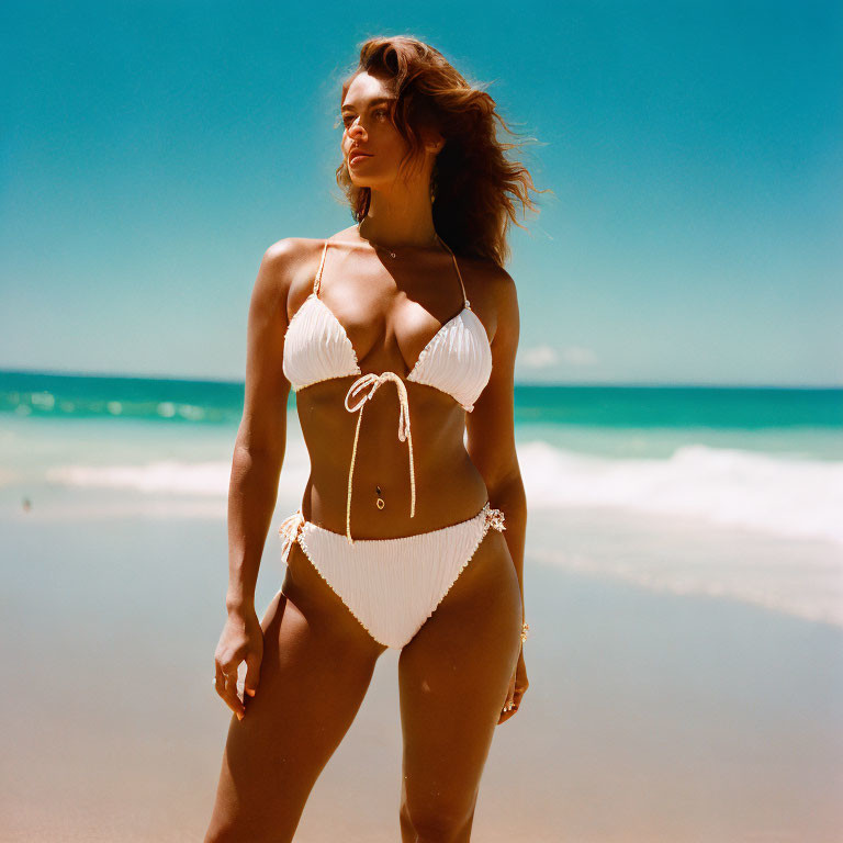 Person in white bikini on sunny beach with turquoise waters.