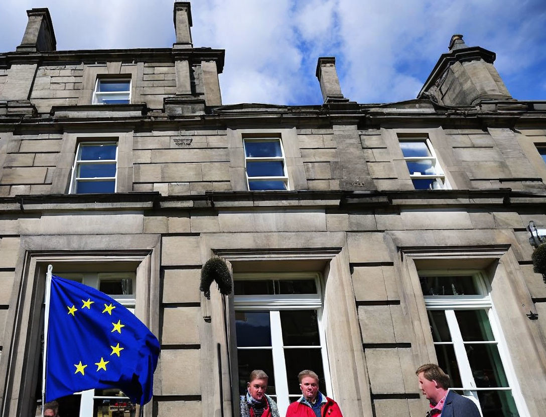 European Union Flag Flutters Outside Stone Building with People Inside