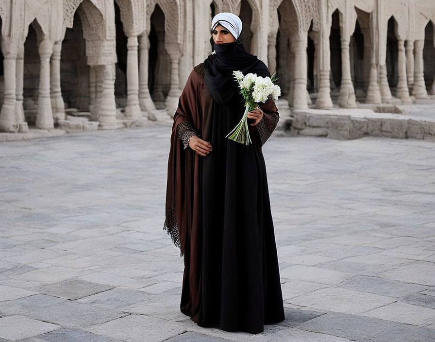 Woman in hijab and abaya with bouquet in ornate arcade courtyard