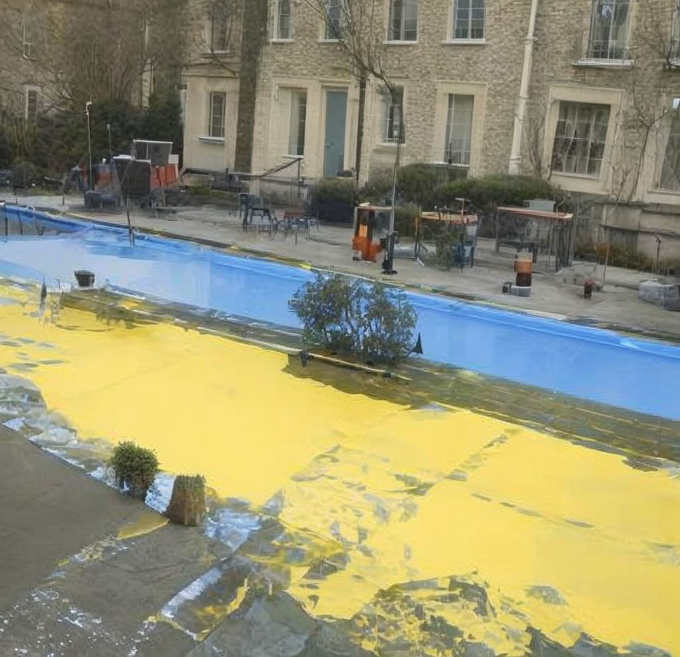 Desolate outdoor pool with cracked yellow ice, buildings, and trees on overcast day