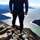 Person admires mountain summit view with fjord, snow-capped peaks, and blue sky