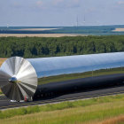 Large grey cylindrical structure on truck near wind turbines and fields.