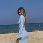 Woman in white dress on beach looking over shoulder with sea and blue sky.