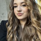 Portrait of woman with long, wavy golden brown hair and green eyes on sparkling background