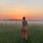 Vintage-dressed person in field at sunset with wildflowers.