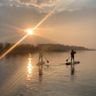 Person rowing boat on calm waters at sunset under warm sky