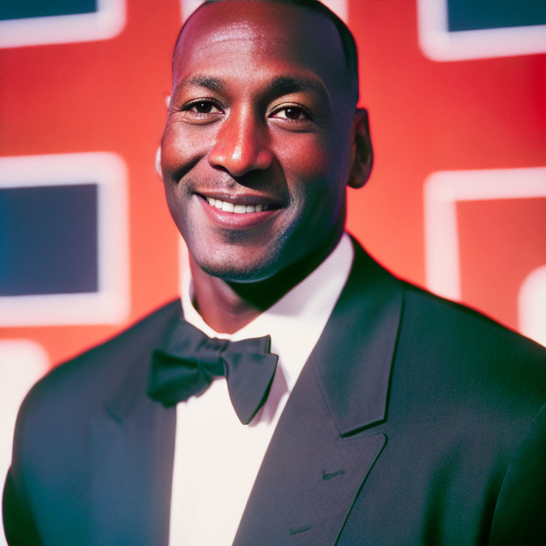 Smiling man in black tuxedo with colorful geometric backdrop