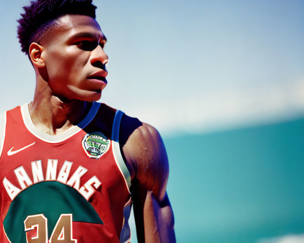 Male athlete in red basketball jersey gazes under clear blue sky