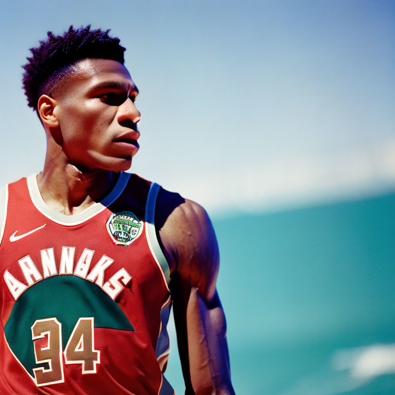 Male athlete in red basketball jersey gazes under clear blue sky