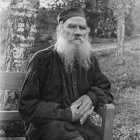 Elderly Man with White Beard in Cap and Glasses Amidst Leafy Foliage