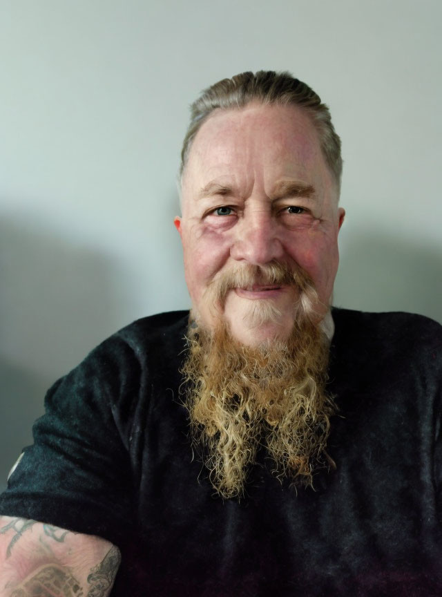 Bearded man with slicked-back hair and arm tattoo