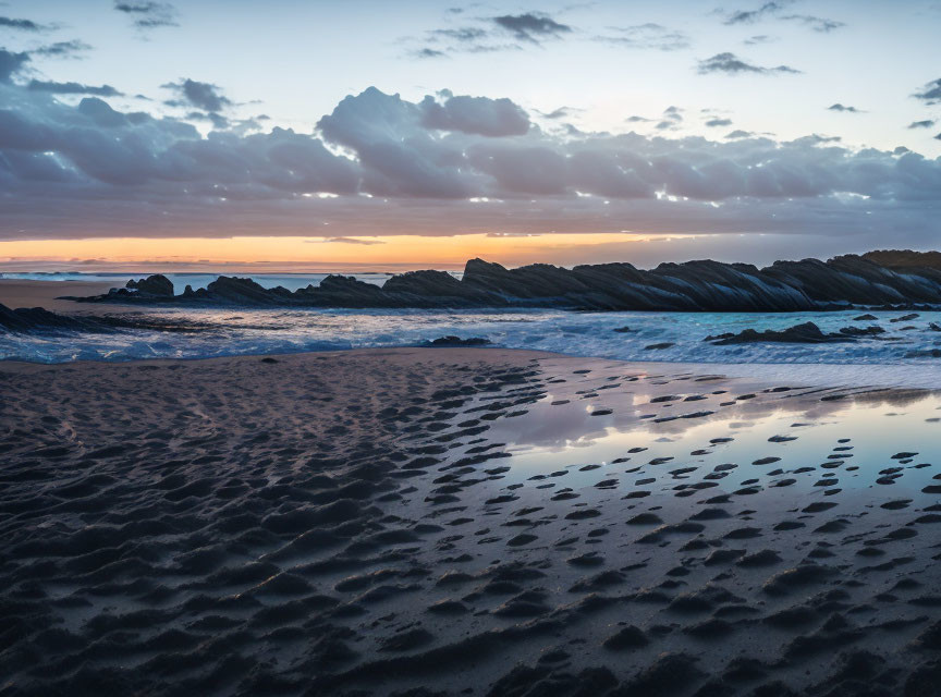 Twilight beach scene with footprints, tide pools, rocks, and colorful sky