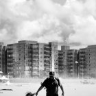 Adult and child walk in desolate urban landscape with dilapidated buildings and birds under cloudy sky