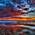 Fiery orange sunset over rocky shoreline with blue clouds