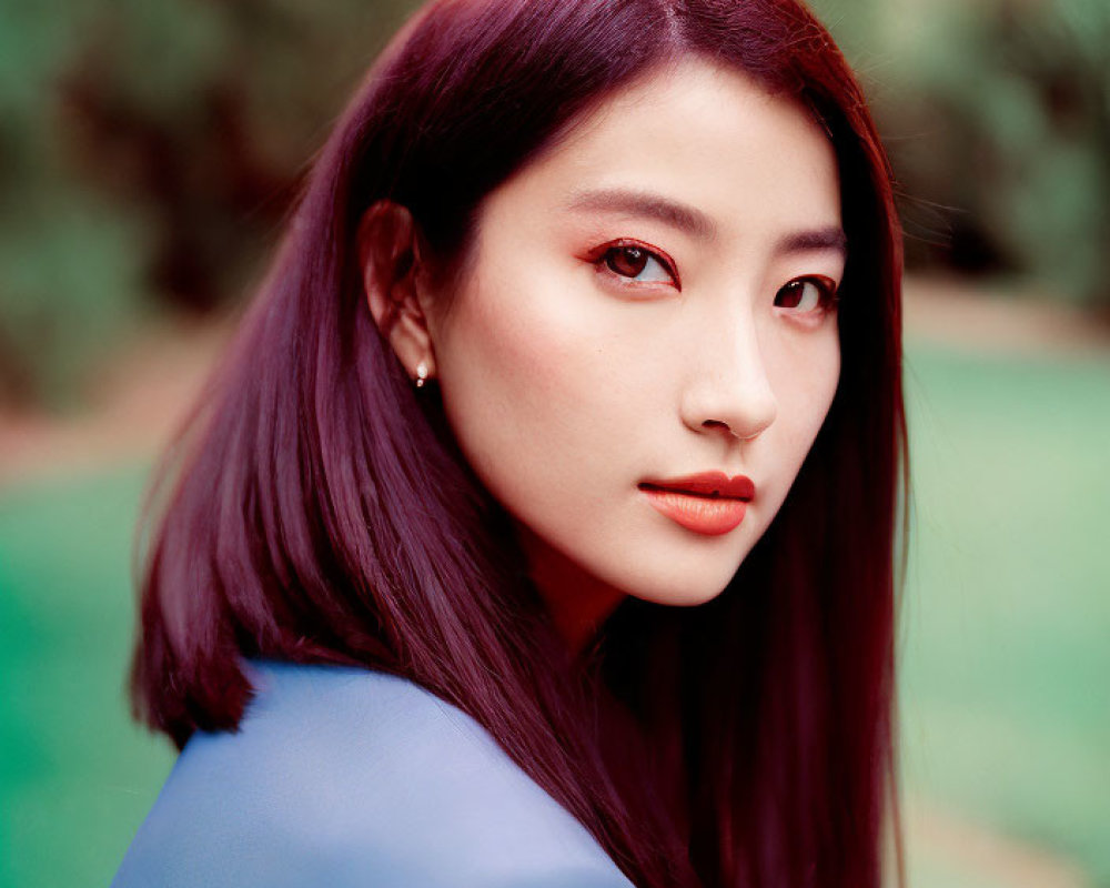 Portrait of woman with dark purple hair and red eyeshadow in blue top on green background