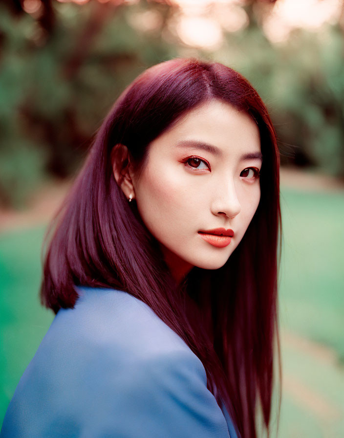 Portrait of woman with dark purple hair and red eyeshadow in blue top on green background