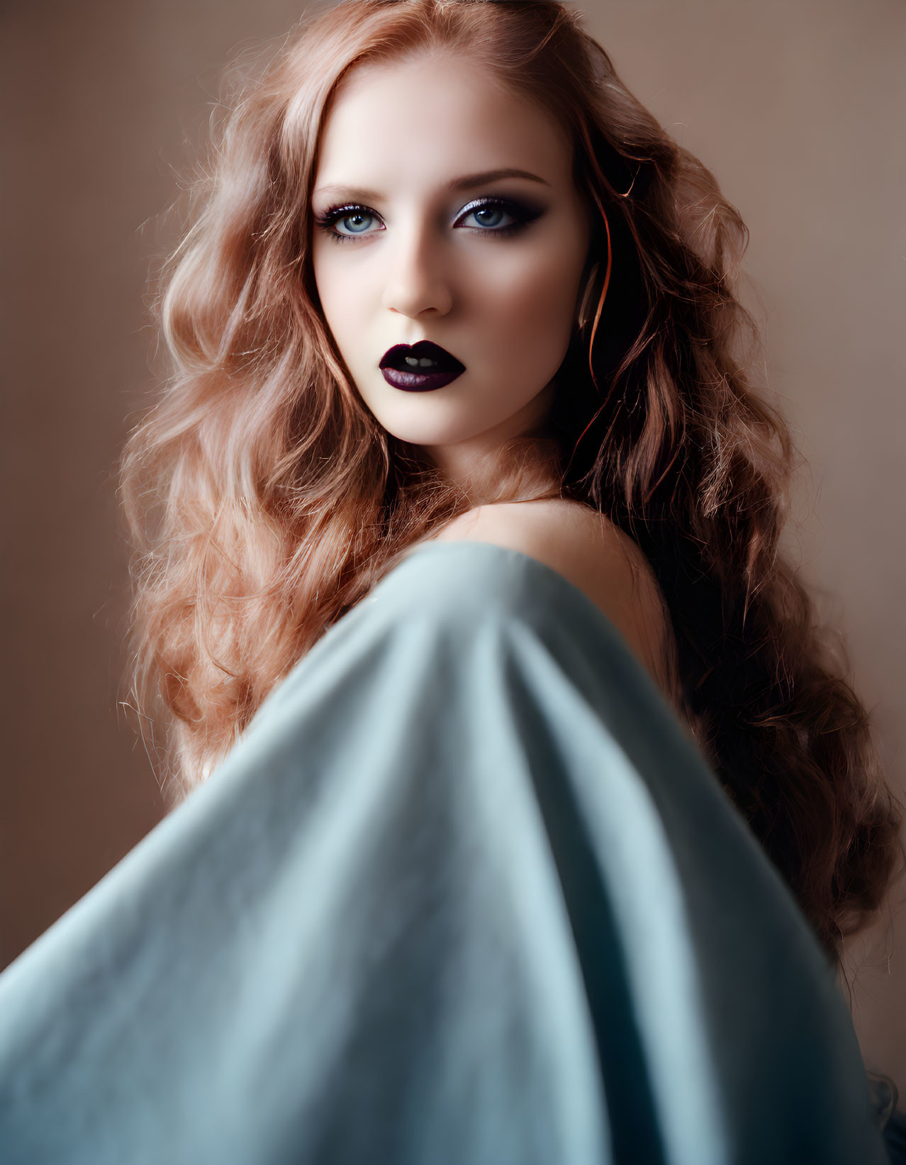 Long-haired woman in dark lipstick gazes intensely over shoulder in draped blue garment