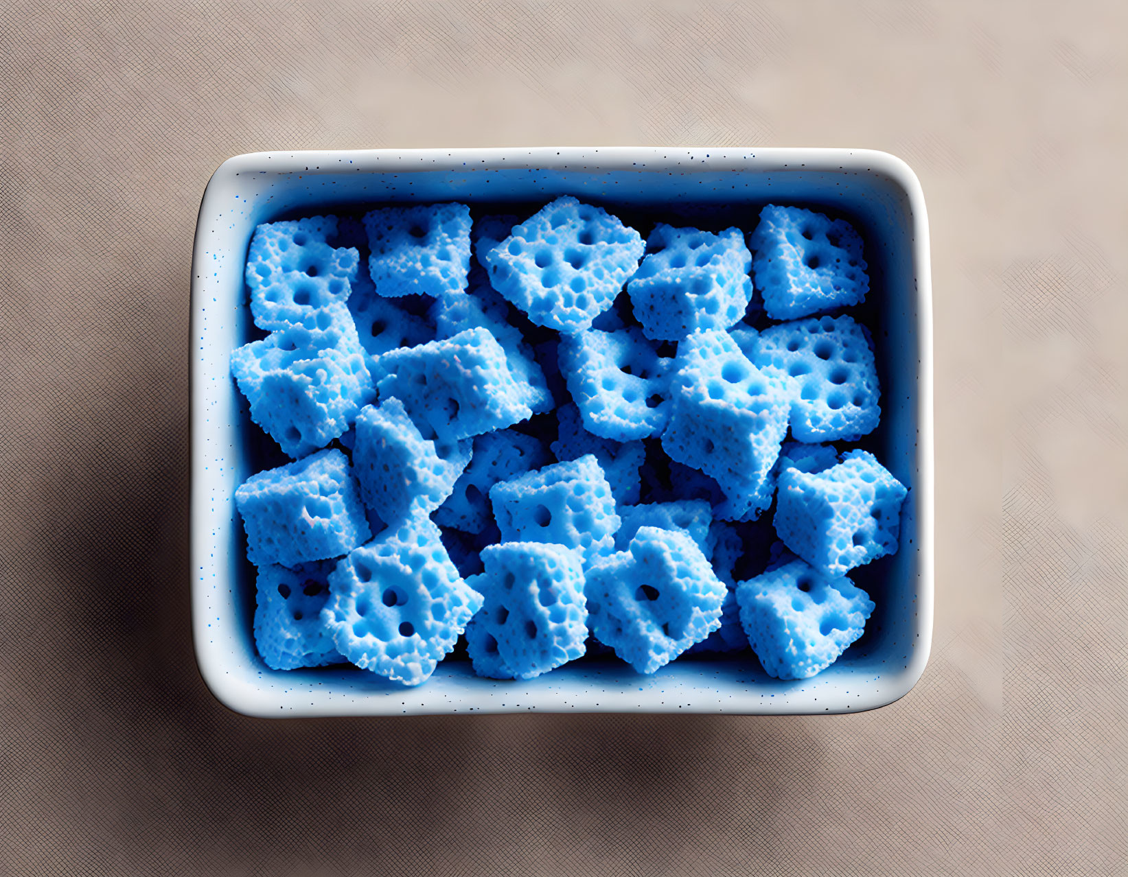 White rectangular bowl with blue star-shaped sponges on beige textured surface