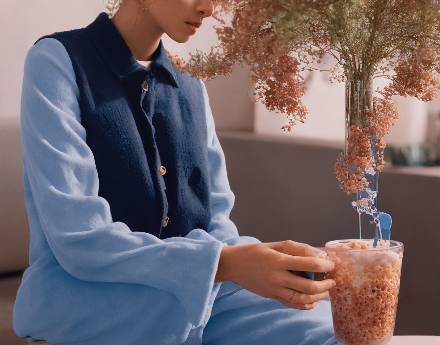 Seated person in blue outfit with frothy drink and dried flowers.