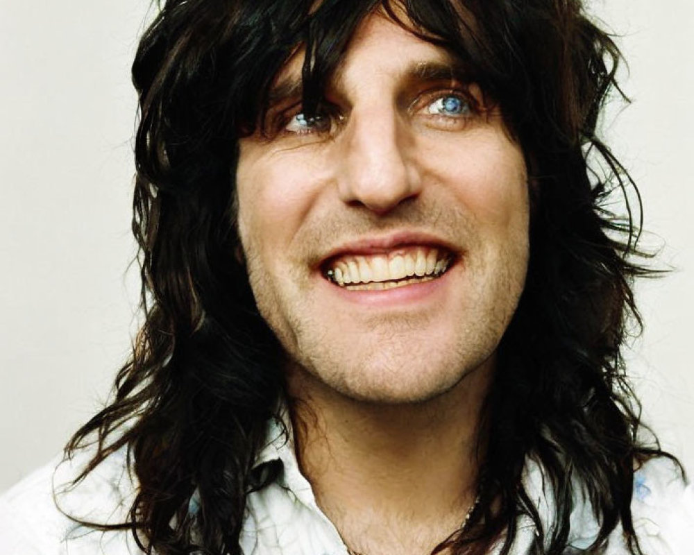 Smiling person with long dark hair, blue eyes, white shirt & necklace