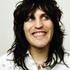 Smiling person with long dark hair, blue eyes, white shirt & necklace