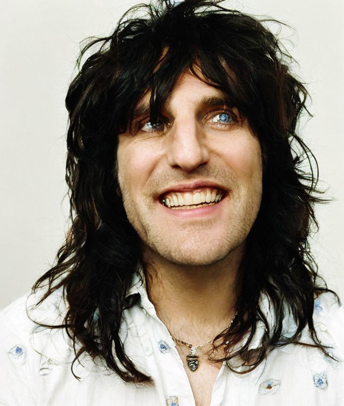 Smiling person with long dark hair, blue eyes, white shirt & necklace